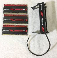 Three Corsair Dominator GT DDR3 RAM modules and one Corsair Airflow fan with power cable laid out on white surface.