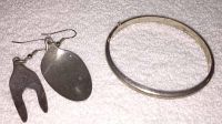 Sterling silver bangle bracelet and two metal earrings on a white textured surface, showing detail of earrings and bracelet clasp.