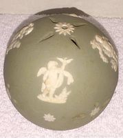 Side angled view of green jasperware pomander showing white cherub relief and floral details on matte surface.