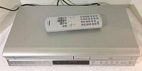 Front view of Toshiba dual deck VCR and DVD player with remote placed on top, silver finish.