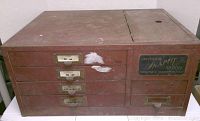 Full view of antique Universal Snap Fit Crystal Company steel storage cabinet with multiple drawers and signs of wear.