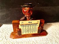 Front view of the hand-carved wooden calendar with the painted bust figure holding the perpetual calendar cards.