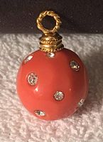 Front view of salmon colored round pendant with clear rhinestones and gold tone twisted bale.