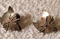Two stylized cat face earrings with cut out details laid on cream fabric background.
