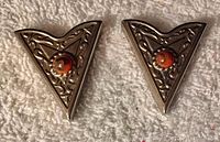 Front view of the pair of triangular silver-toned collar tips with filigree and orange center stone.