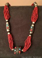 Front view of necklace showing multiple strands of red beads, silver-tone ornamental beads with turquoise and coral colored stones.