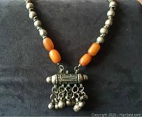 Full view of chunky necklace with silvertone beads and orange-amber colored beads strung together, central pendant with dangling bells.