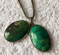 Close-up photo of two green oval stones set in silver-tone bezels on a heishi bead chain.