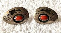 Front view of pair of Native American style oval shadow box post earrings with bear claw pierced design and coral stone center on textured white background.
