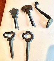 Full view showing all 5 items: 4 unique screw bolts with different ornamental tops and 1 curved hanging hook.