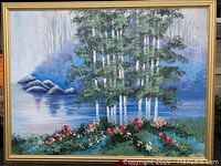 Full view of framed oil painting featuring trees, water, rocks, and flowers in landscape style.