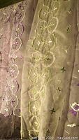 Close-up image showing sheer fabric dresser scarf with green and purple floral embroidery down length