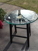 Side table outside, showing full round glass top and black wooden frame.