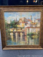 Framed oil painting of cityscape with buildings, bridge and water reflections.