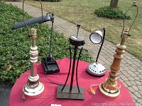Five lamps arranged on table outdoors: two desk lamps, one with radio controls and remote, and three tall traditional table lamps with wood and brass finishes.
