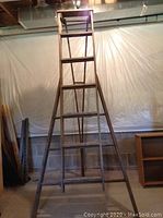 Front view of antique wooden farm ladder showing its height, wide base, and multiple rungs.