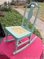 Full view of an antique rocking chair painted light green, showing the full chair including the curved rocker legs and decorative backrest.