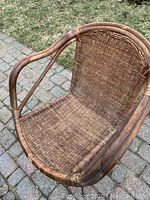 Front angled view of the mid century modern woven rattan chair highlighting curved armrests and woven seat.