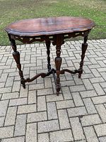 Front angle view of antique wooden side table showing ornate carved legs and scrolled edges to the top.