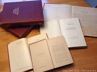 Two volumes of The Century Appleton Dictionary with maroon covers and gold embossed titles with multiple other antique books opened to title and preface pages spread on table surface.