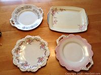 Four assorted vintage cake and serving plates arranged on wood table showing varied shapes and floral patterns