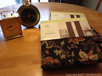 Two clocks and packaged curtain panels on wooden table: Hamilton rectangular carriage clock, West Germany oversized pocket watch-style clock, and two curtain panels still in original packaging