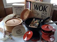 Full lot showing the boxed bamboo steamer, bamboo steamers, hand hammered wok, and vintage red serving dishes with lids.