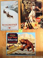 Set of three vintage style metal tin signs with hunting and ammunition themes placed on wooden floor.