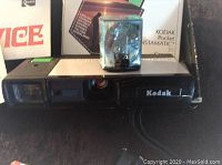 Kodak Pocket Instamatic 30 camera with clear blue flash cube positioned on top, original box behind