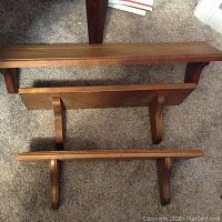 Three wooden shelves stacked vertically showing front and top surfaces and curved support brackets beneath each shelf.