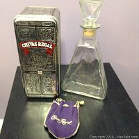 Closed embossed Chivas Regal 12 Years metal tin with embossed designs and red banners, next to glass decanter and Crown Royal purple velvet satchel.