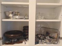 Top shelf with footed silver bowl, silver butter dishes, glass bowls, and salt and pepper sets on lower shelves.