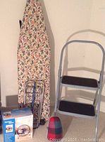 Full lot overview showing ironing board, step stool, boxed fan, door stop, and luggage cart.