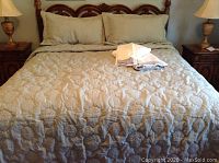 King size beige quilted damask comforter on bed with matching shams and two pillows with folded sheets on top