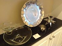 Photo showing all items on a black countertop: Wilton Armetale pewter plate on stand, Jefferson Cup, glass chip and dip set with gold-tone stand, mirrored star sculpture