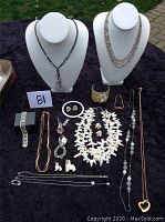 Full lot including necklaces displayed on busts, bracelets, watches, earrings, and pins laid out on black cloth outdoors.