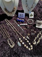Photo showing an assortment of ladies' jewelry items laid on table including necklaces on busts, bracelets, watches, pins, and earrings.