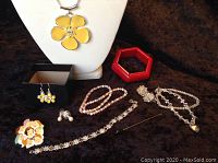 Full view of costume jewelry lot including yellow flower pendant necklace, yellow flower earrings, pink and white beaded bracelet, cluster earrings, clear crystal necklace with heart pendant, Disney 7 Dwarfs pin, red hexagonal bangle, and stick pin.
