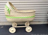 Side profile of vintage wicker bassinet showing curved hood, green ribbon, and wooden wheels.