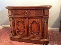 Front view of one Thomasville nightstand showing drawer and cabinet doors with decorative carved panels and brass ring pull