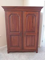 Front view of closed armoire showing double paneled doors, decorative molding, and metal handles.