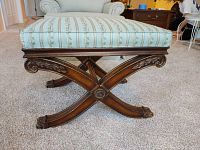 Side view of bench showing carved crossed wooden legs with claw feet and light blue striped floral fabric upholstery.