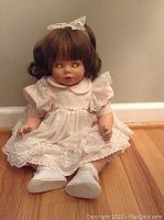 Front seated view of a collectible Susan Wakeen doll dressed in pink and white lace dress, showing face, hair, and footwear.