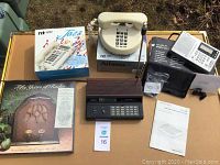 Overview of all items on wooden table showing phone, radio display plaque, and World Receiver radio with accessories.