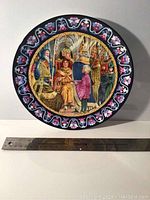 Front view of one Wedgwood plate showing colorful historical themed scene with ornate blue and pink border, next to 12-inch ruler for size.