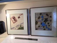 Two framed artworks side by side on a shelf with ruler below