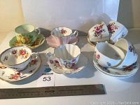 Photo of 8 assorted floral teacup sets with saucers arranged with a ruler for scale