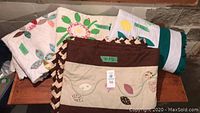 Four handmade quilts folded and laid out showing different styles and color schemes including floral and leaf appliqué and patchwork.