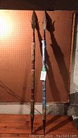 Full length photo of two long decorative spears leaning against pegboard wall showing overall length and design.