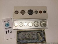 Two Canadian coin sets and a 1954 Canadian five dollar bill laid out on a flat surface.